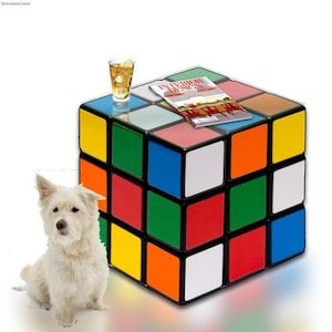 a white dog sitting next to a rubik cube with a shot glass on top