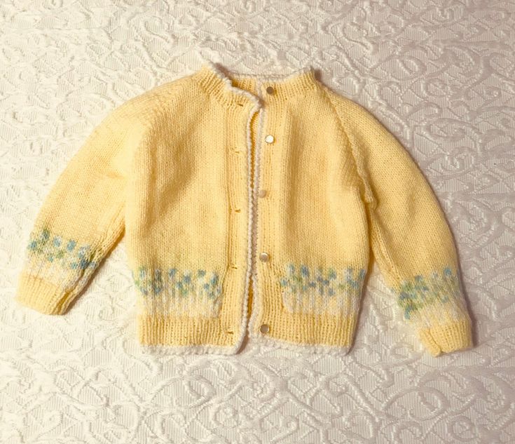 a yellow cardigan sweater with blue flowers on the front and green leaves on the back