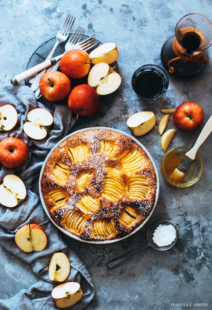 an apple pie with powdered sugar on top next to sliced apples and silverware