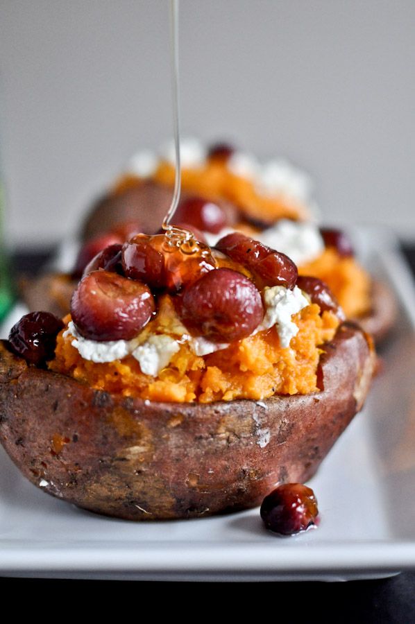 baked potatoes with grapes and goat cheese being drizzled over them on a plate