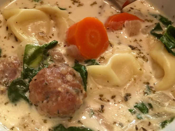 a white bowl filled with pasta and meatballs covered in cheese, spinach and carrots