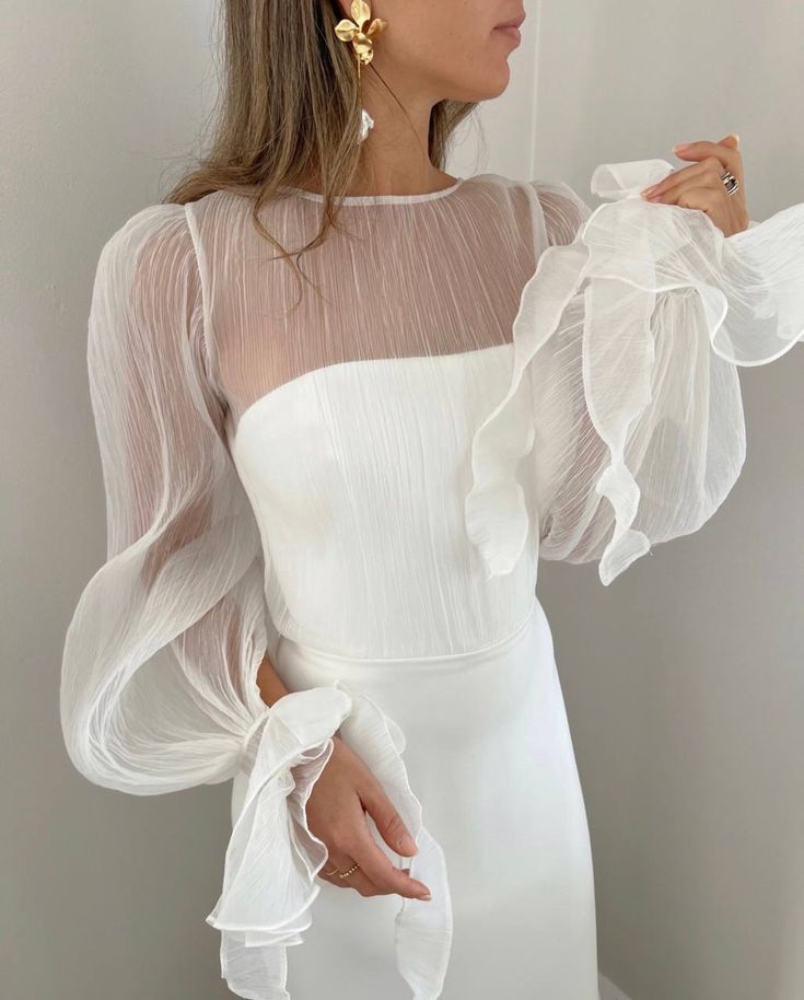 a woman wearing a white dress with sheer sleeves