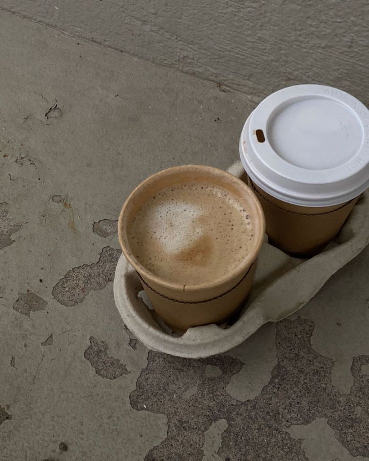 two coffee cups sitting on top of each other in front of a cement wall and floor