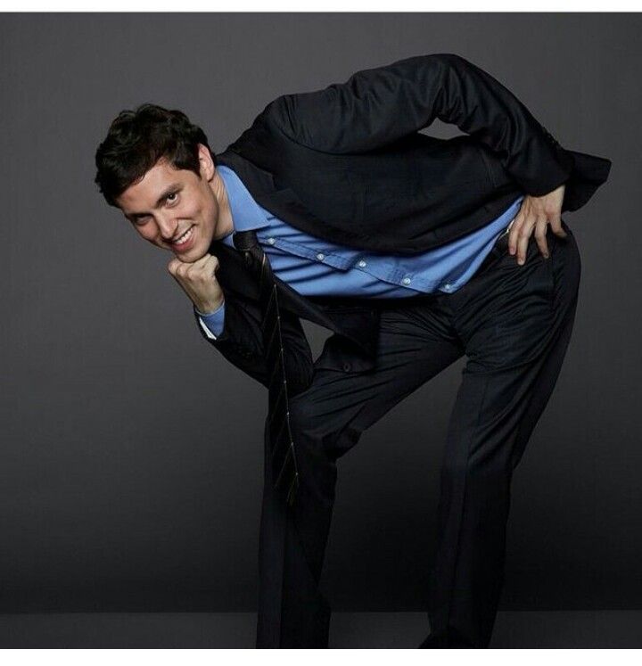 a man in a black suit and blue shirt is posing for a photo with his hands on his hips