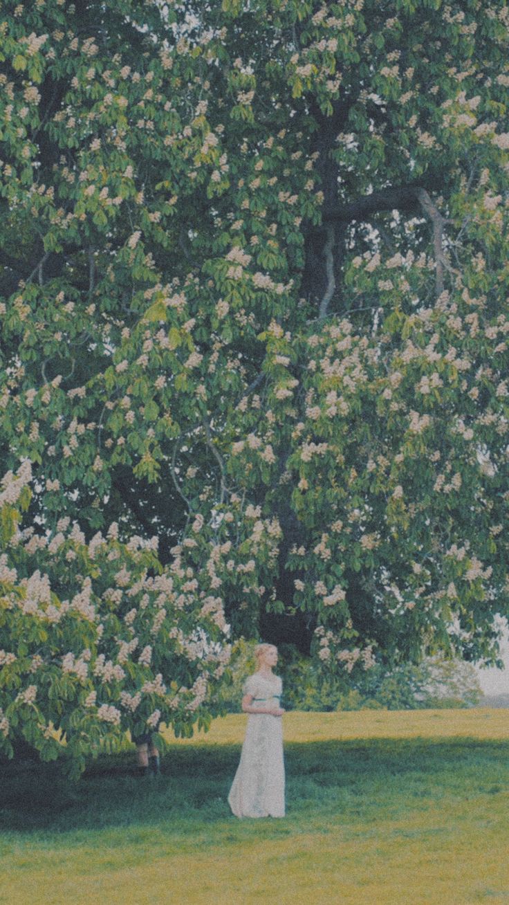 a woman in a white dress standing under a large tree with lots of flowers on it