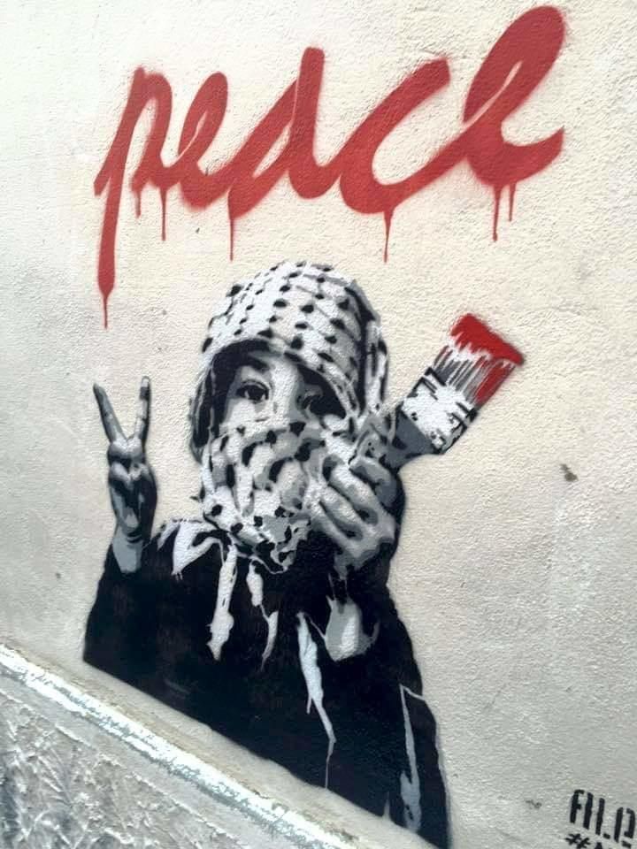 a person holding a paintbrush in front of a wall with the word peace painted on it