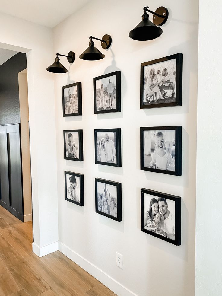 black and white photographs are hung on the wall next to two lamps in this hallway