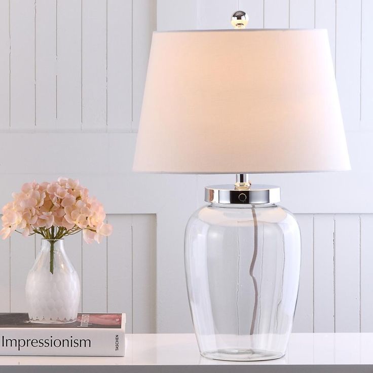 a table lamp sitting on top of a desk next to a vase with flowers in it