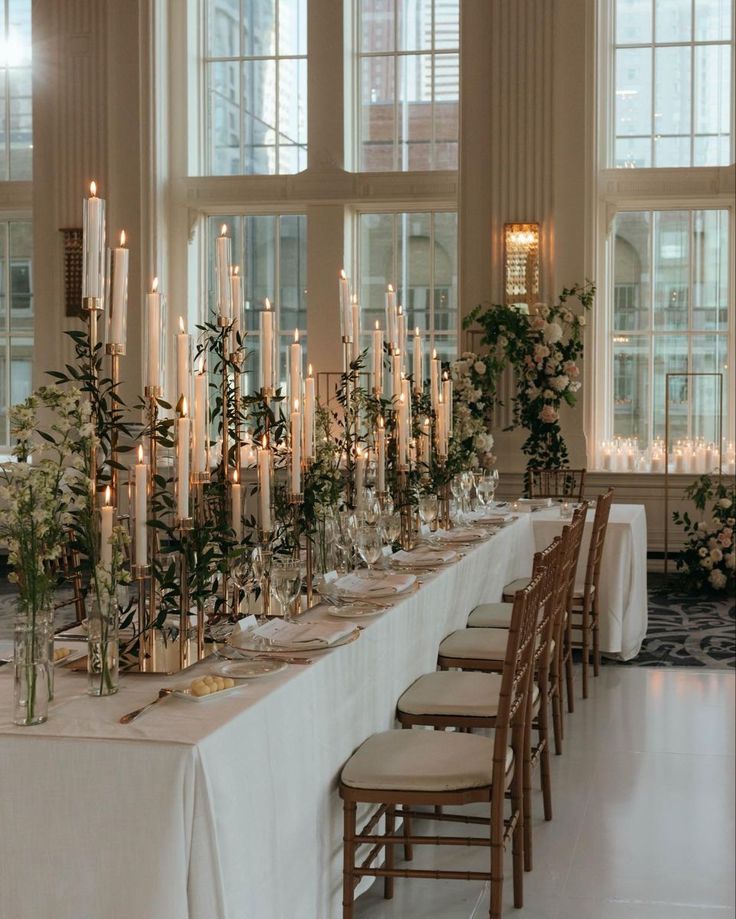 a long table with candles and flowers on it in a large room filled with windows