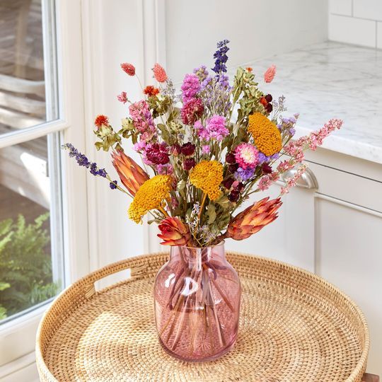 a vase filled with flowers sitting on top of a wicker table next to a window