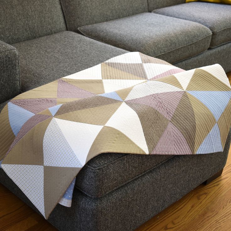 a couch with a blanket sitting on top of it next to a gray couch and wooden floor