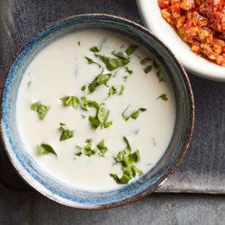 two bowls filled with soup next to each other on a tablecloth covered tray and another bowl full of food in the background