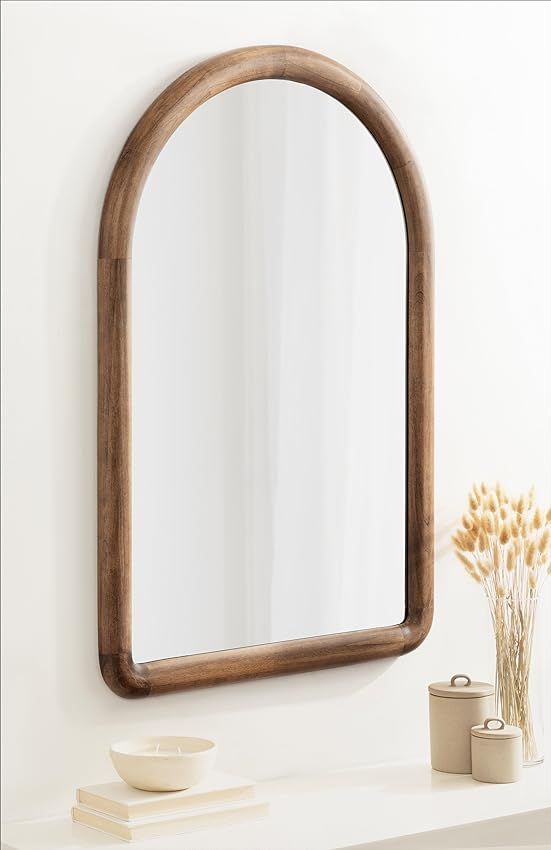 a mirror sitting on top of a white counter next to a vase and plant in front of it