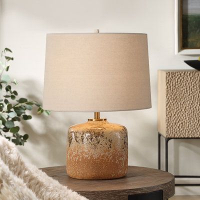 a table lamp sitting on top of a wooden table next to a white rug and potted plant