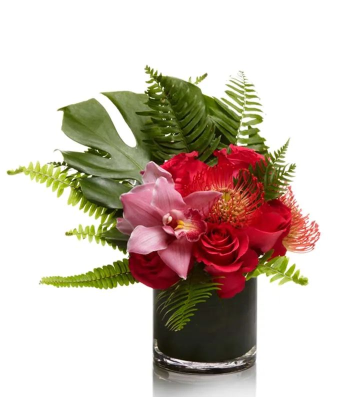 a vase filled with red and pink flowers on top of a white table next to green leaves