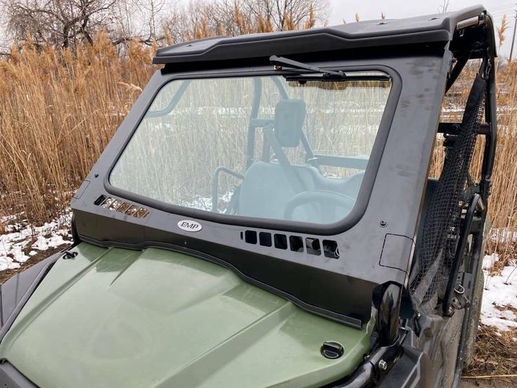 a green utility vehicle parked on the side of a road in front of tall grass