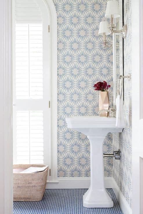 a bathroom with blue and white wallpaper, a pedestal sink and large window in the corner