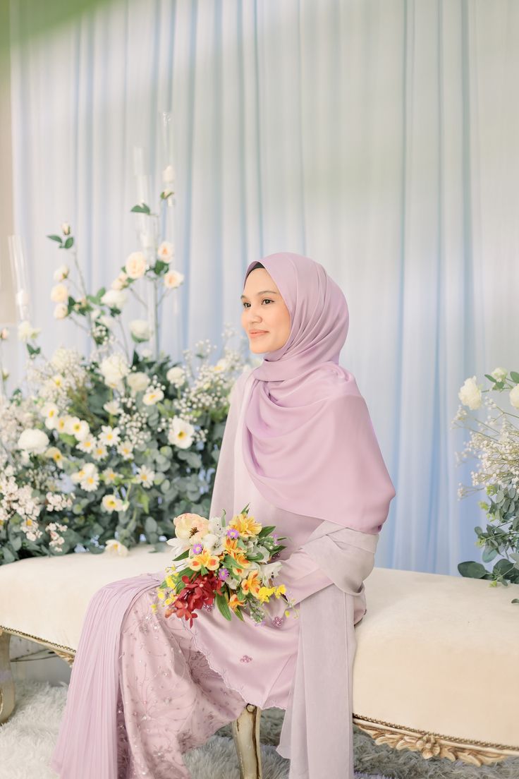 a woman wearing a hijab sitting on a bench with flowers in the background