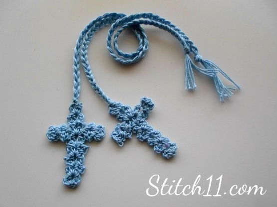 a crocheted blue cross with tassels on a white surface