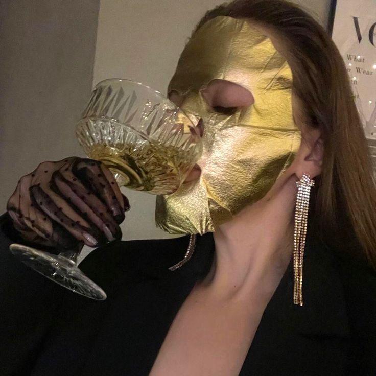 a woman wearing a gold mask drinking from a wine glass