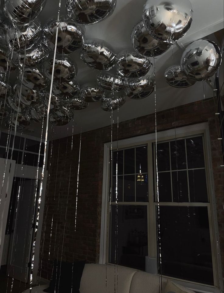 a living room filled with lots of shiny silver balloons hanging from the ceiling over a couch