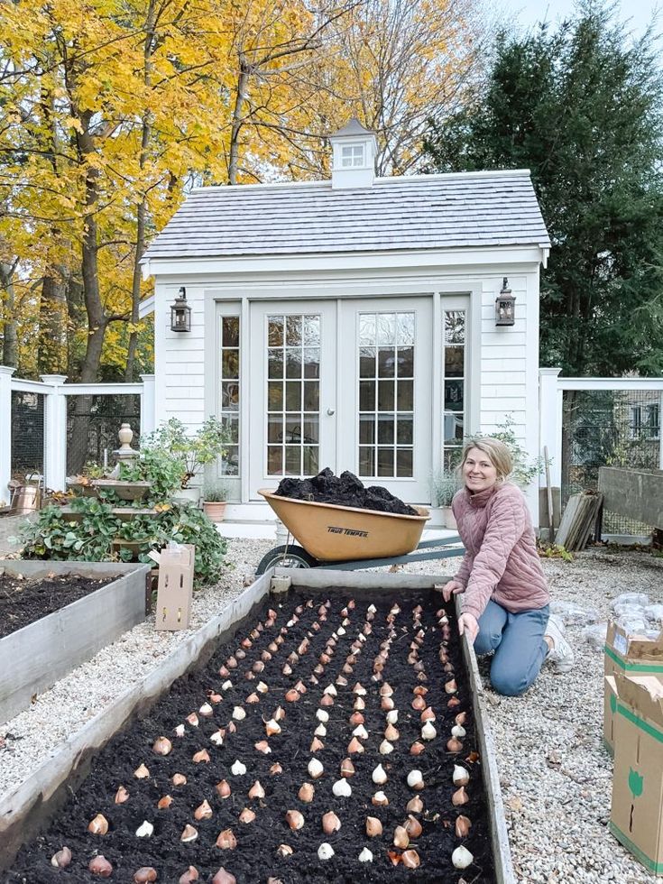 a woman kneeling down in front of a garden bed filled with dirt and small chickens