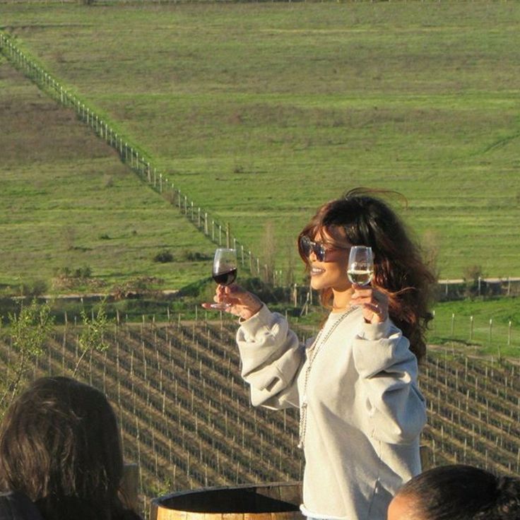 a woman holding up two wine glasses in front of her face while standing next to a barrel