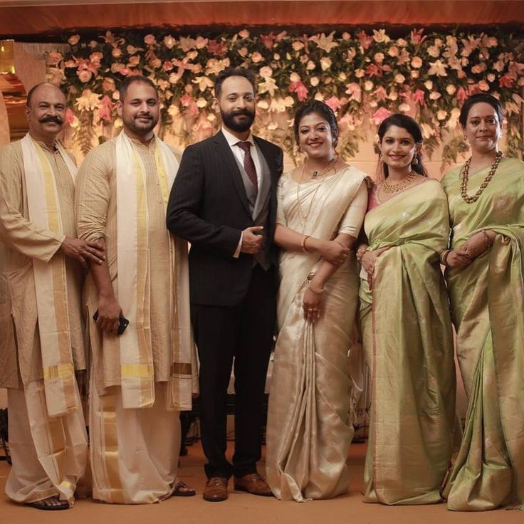 a group of people standing next to each other in front of a wall with flowers