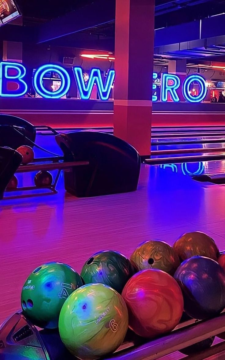 bowling balls are lined up in a row at the bowling alley with neon signs behind them