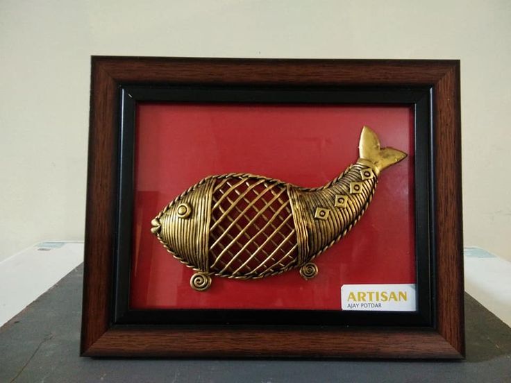 a red and black frame with a gold fish in it's mouth on a table