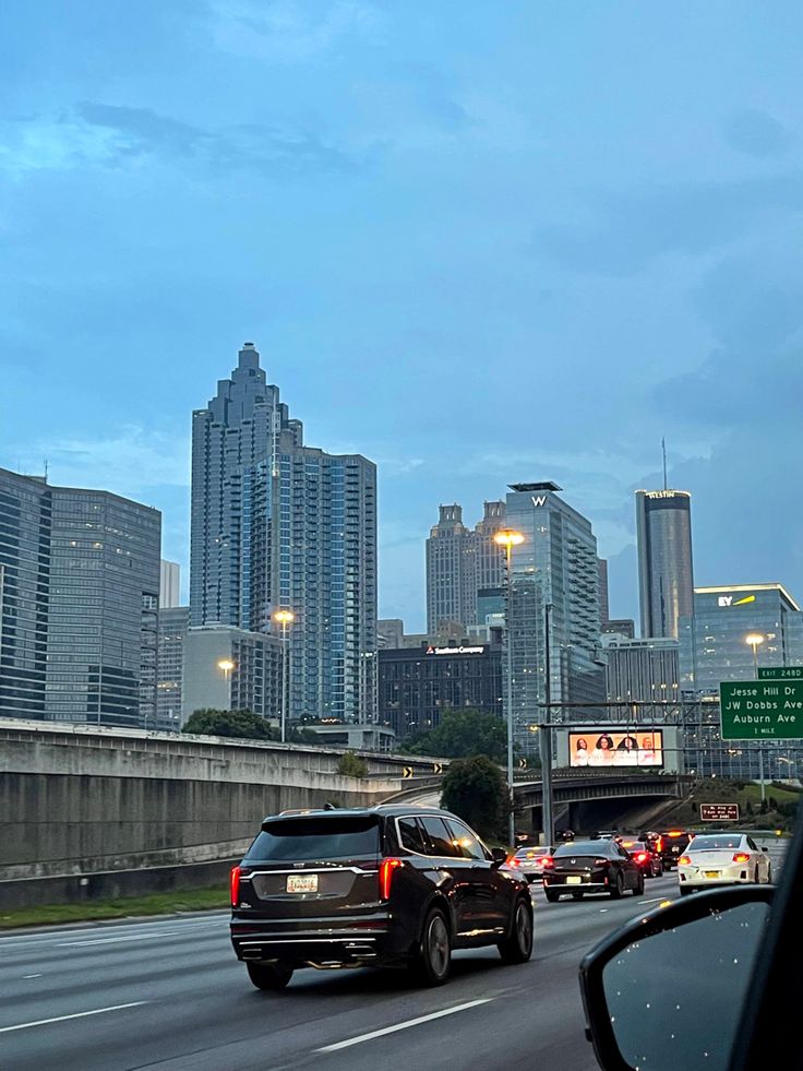 cars are driving down the highway in front of tall buildings and skyscrapers at dusk