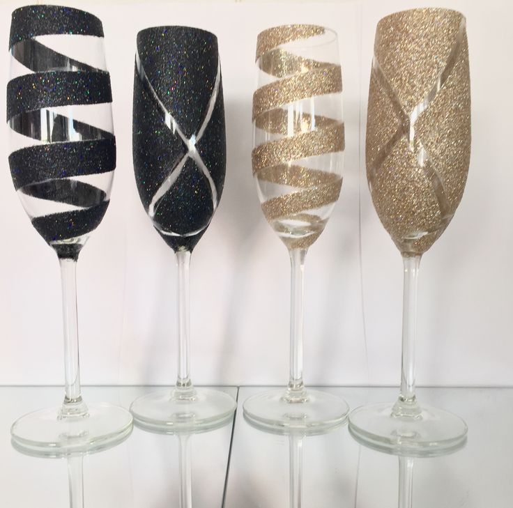 four wine glasses with gold and black glitter ribbons on the rims are lined up against a white wall