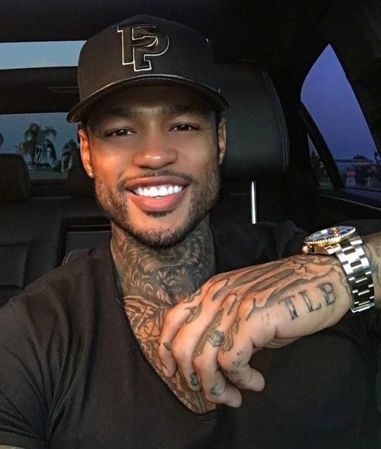 a man with tattoos on his arm and wrist sitting in the back seat of a car