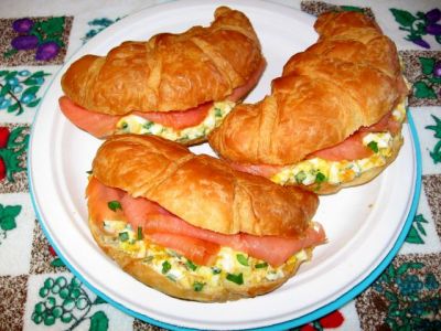 two croissants with eggs and ham are on a white plate next to a flowered tablecloth