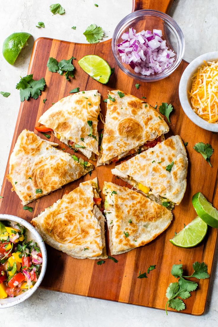 a wooden cutting board topped with quesadilla cut into eight slices next to bowls of salsa