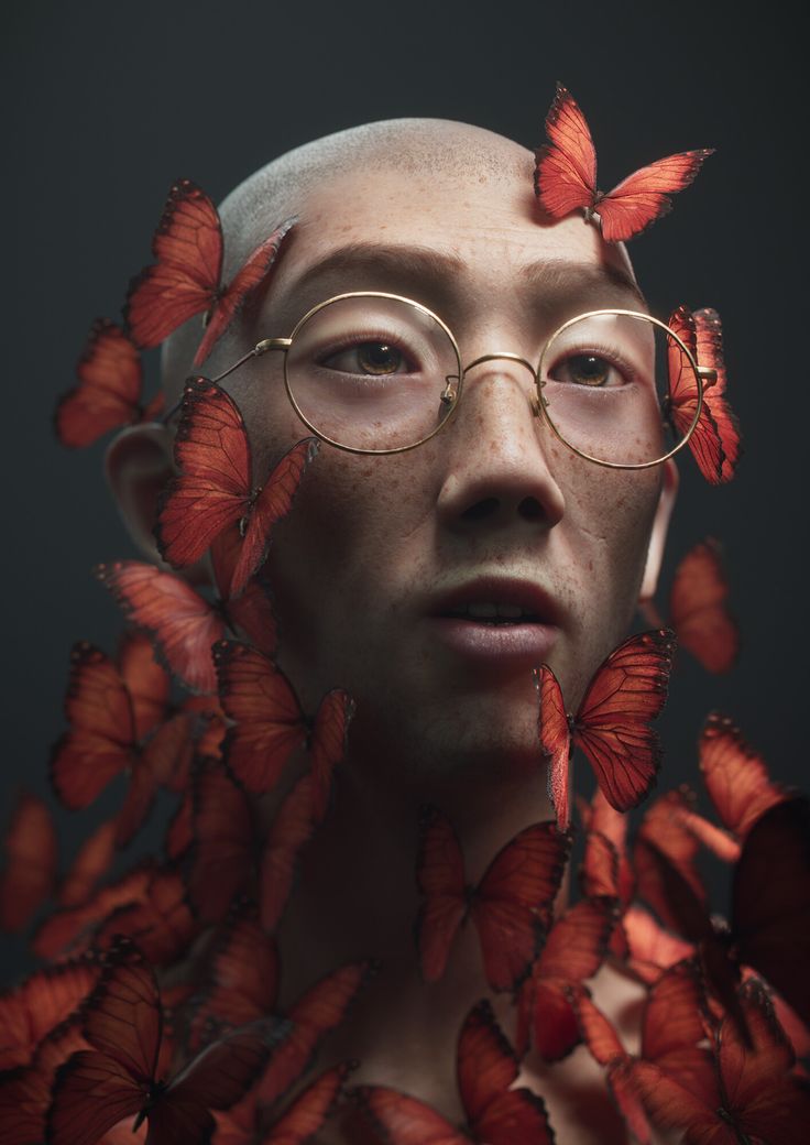 a man with glasses and butterflies on his head is staring at the camera while he's surrounded by red butterflies