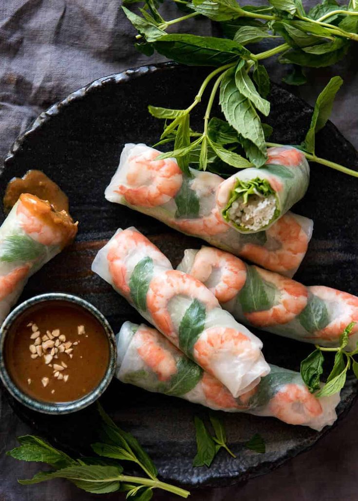 shrimp spring rolls with dipping sauce on a black platter next to greens and seasoning