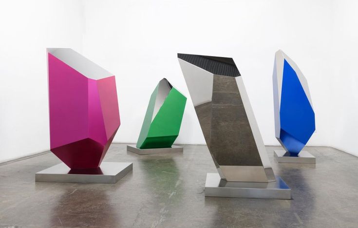 three different colored sculptures are on display in a room with white walls and concrete flooring