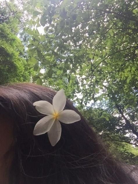 a woman's head with a white flower on it and trees in the background