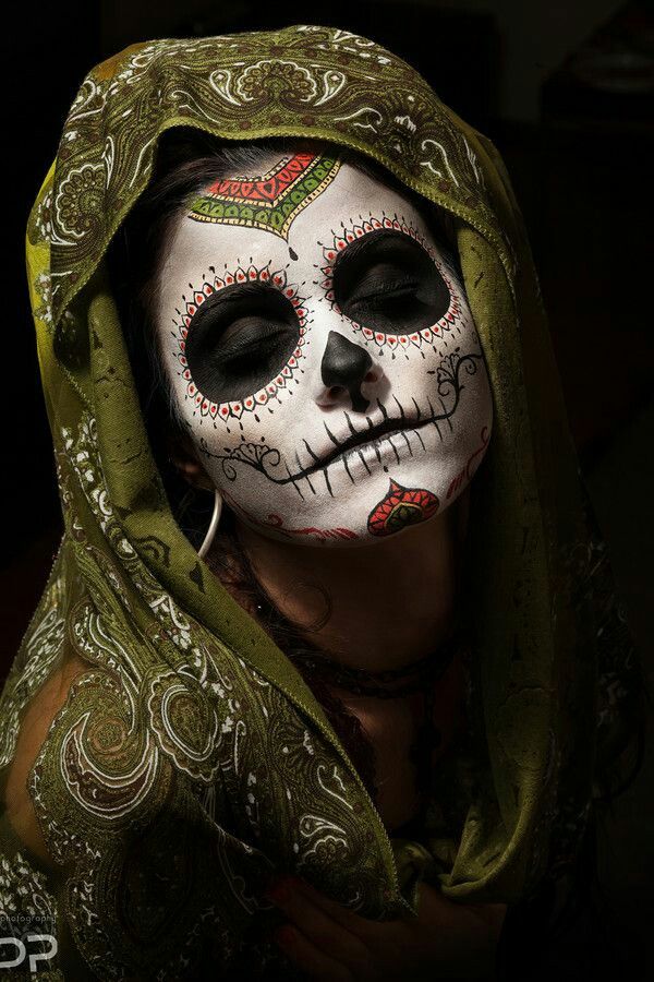 a woman with makeup painted to look like a skeleton wearing a green scarf and headdress