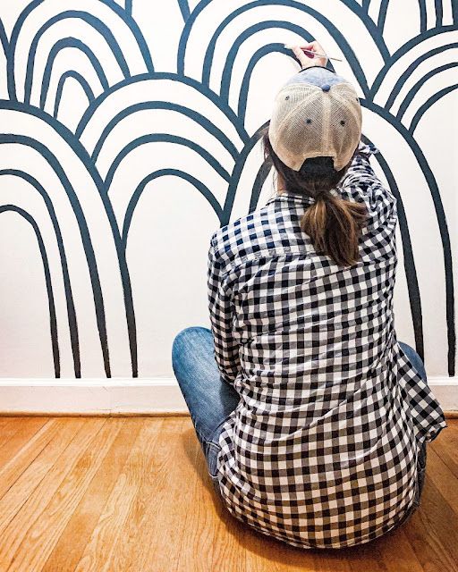 a woman sitting on the floor in front of a wall with black and white designs