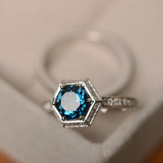 an engagement ring with a blue topaz surrounded by white diamonds in a gift box