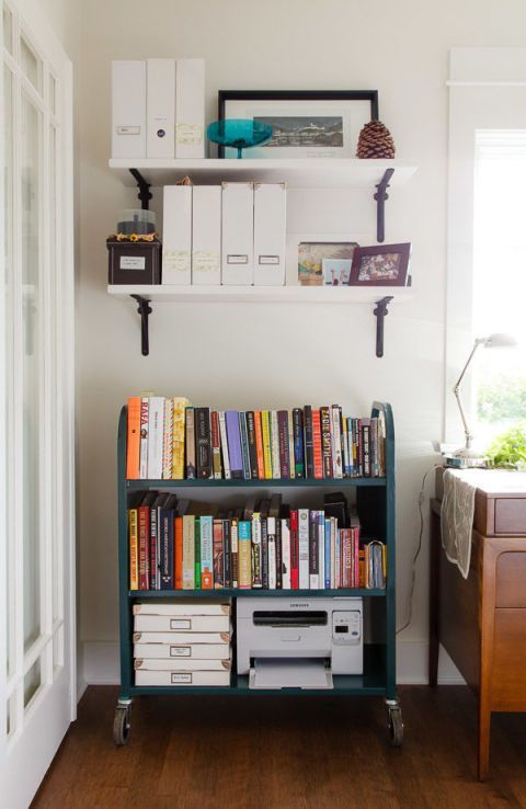 a bookshelf filled with lots of books next to a dresser and desk in a room