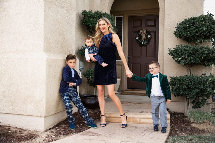 a woman and two boys are standing in front of a house