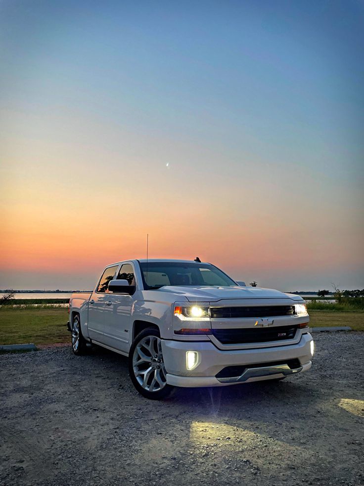 a white truck parked on top of a dirt field next to the ocean at sunset