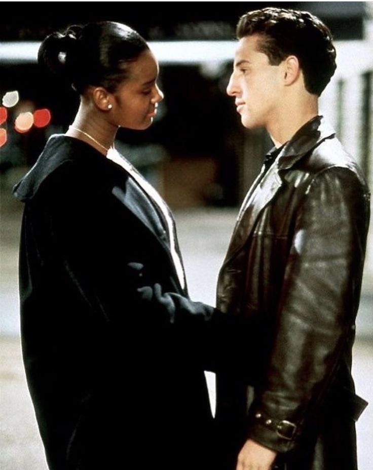 a man and woman standing next to each other on a street corner, facing each other