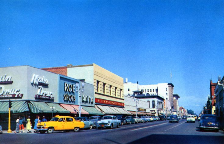 an old photo of cars parked on the side of the road in front of stores