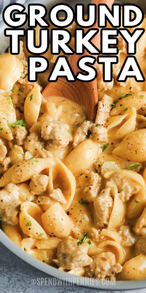 a white bowl filled with pasta covered in chicken and sauce next to a wooden spoon