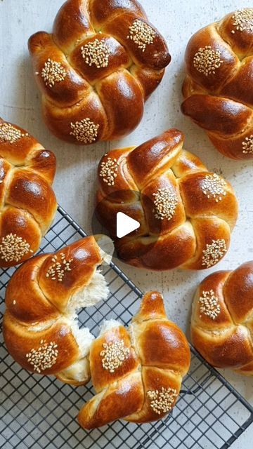 several hot cross buns on a cooling rack with one cut in half and the other topped with sesame seeds