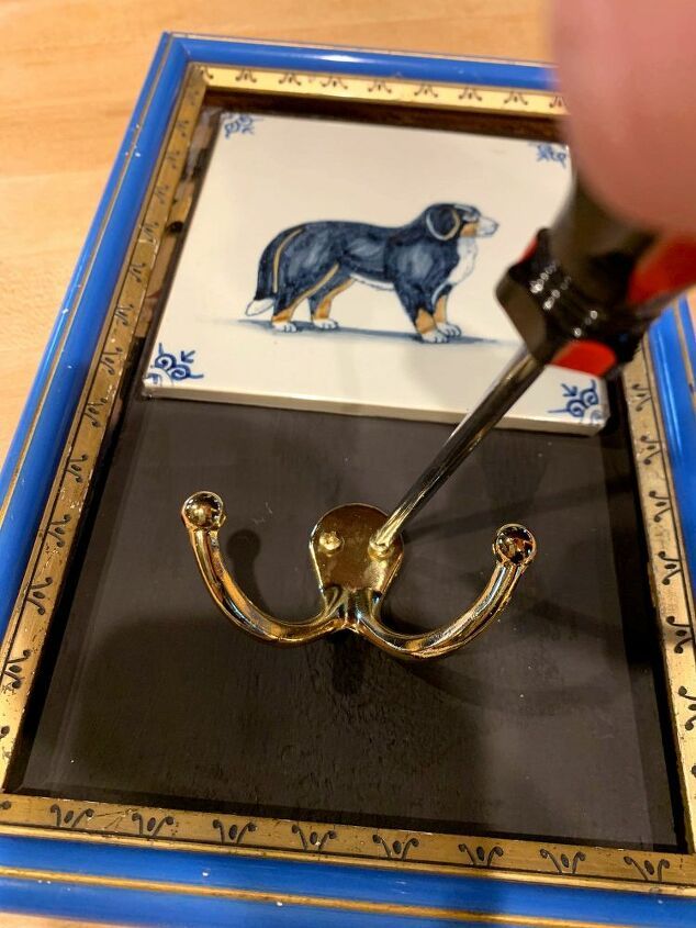 a person is holding a paintbrush and painting a dog on a tile with gold trim